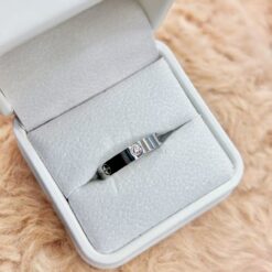 Metal ring with a small diamond displayed in a soft gray jewelry box on a fluffy beige surface, photographed from above.