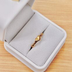 Gold jewelry piece resting in a gray padded jewelry box, on a wooden table surface, showcasing a shiny link-like design.