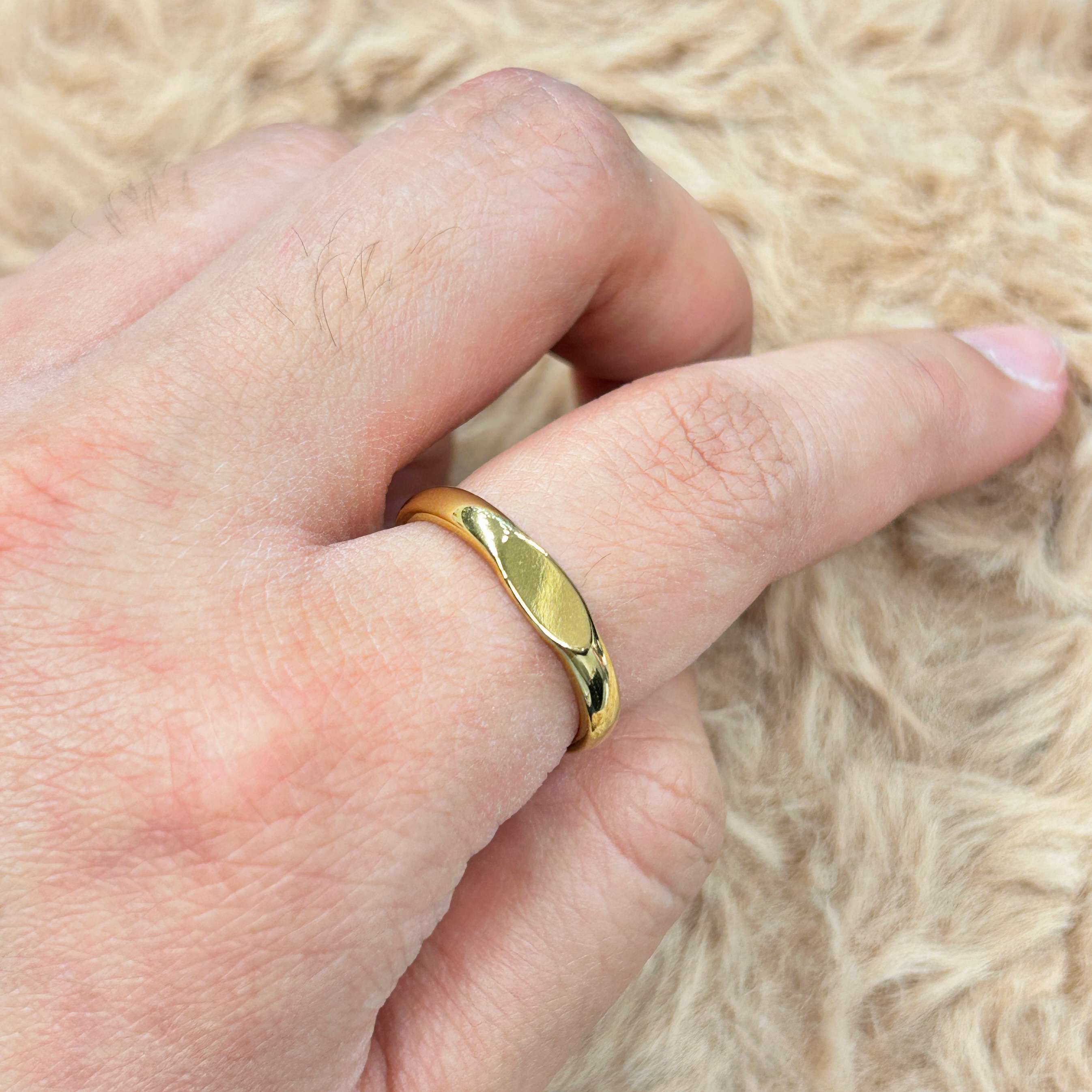Close-up of a finger wearing a gold ring with a green inset, resting on a soft beige fabric background.