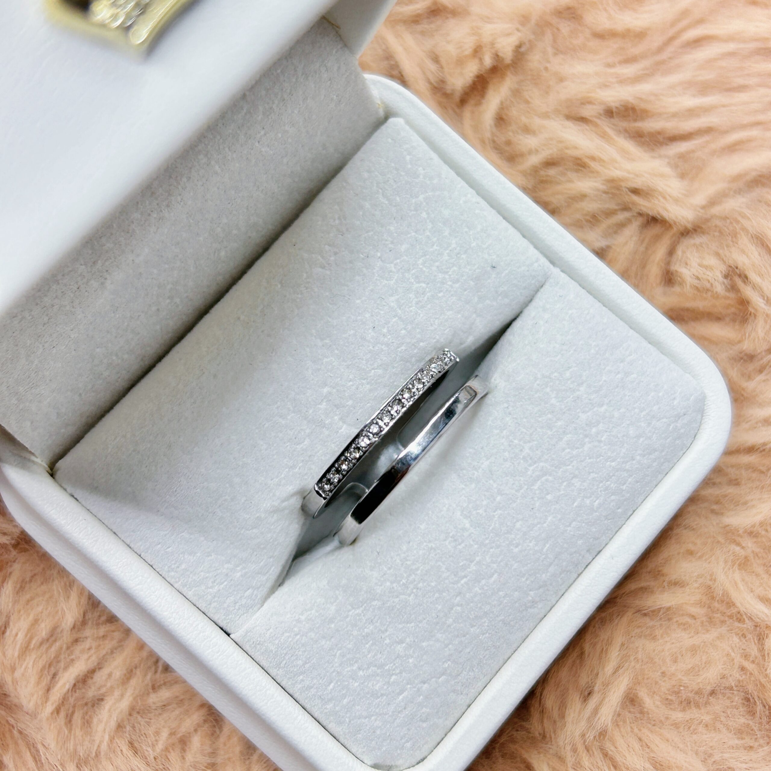 Diamond-studded engagement ring in a silver band resting in a gray velvet jewelry box on a fur background.