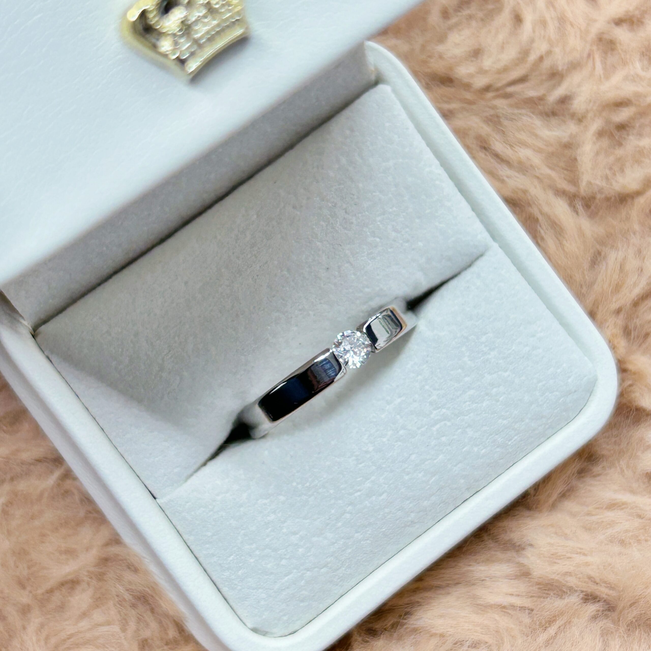 Diamond ring nestled in a light blue velvet jewelry box on a fluffy brown surface, close-up view.