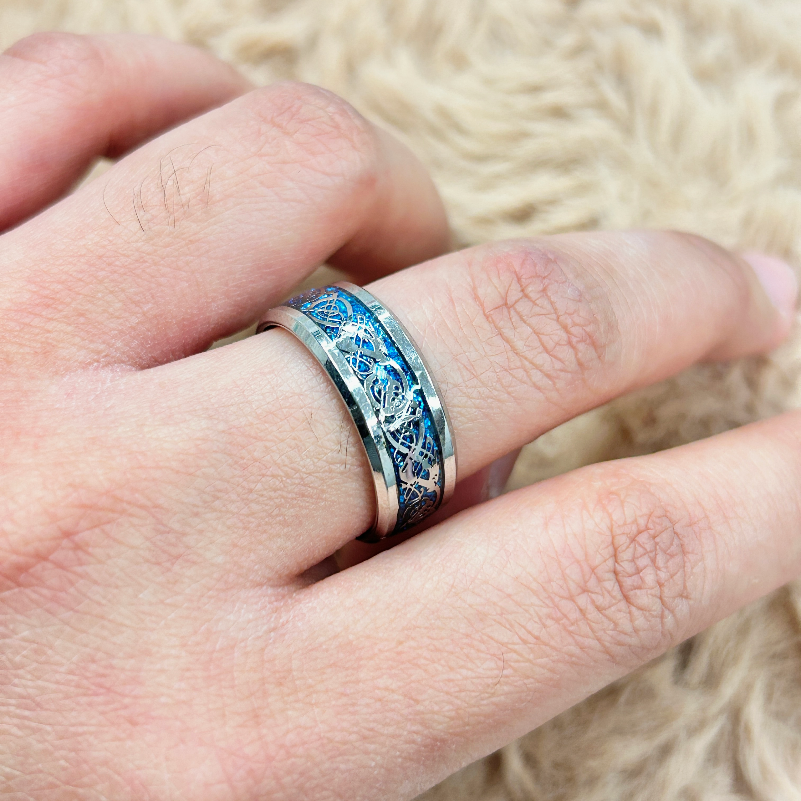 Close-up of a finger wearing a silver ring with a blue ornate pattern on a decorative band