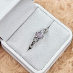Close-up of a silver ring featuring a purple oval gemstone and small diamonds in a gray jewelry box on fur.