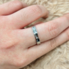 Close-up of a silver triple-band ring on a finger with textured skin and light hair, resting on a soft beige surface.