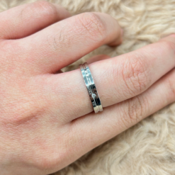Close-up of a silver triple-band ring on a finger with textured skin and light hair, resting on a soft beige surface.