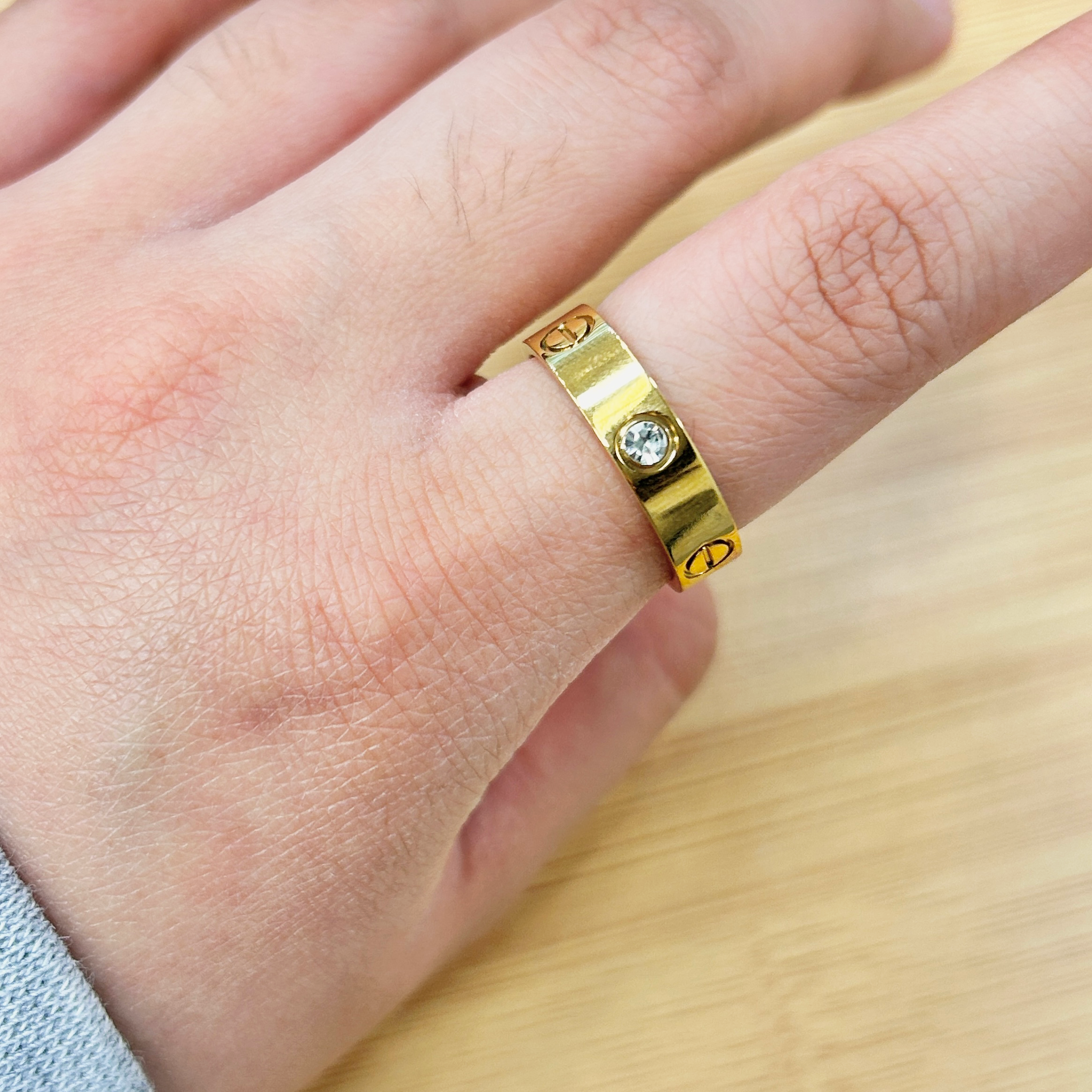 Close-up of a hand wearing a wide gold ring with small embedded stones on the finger.
