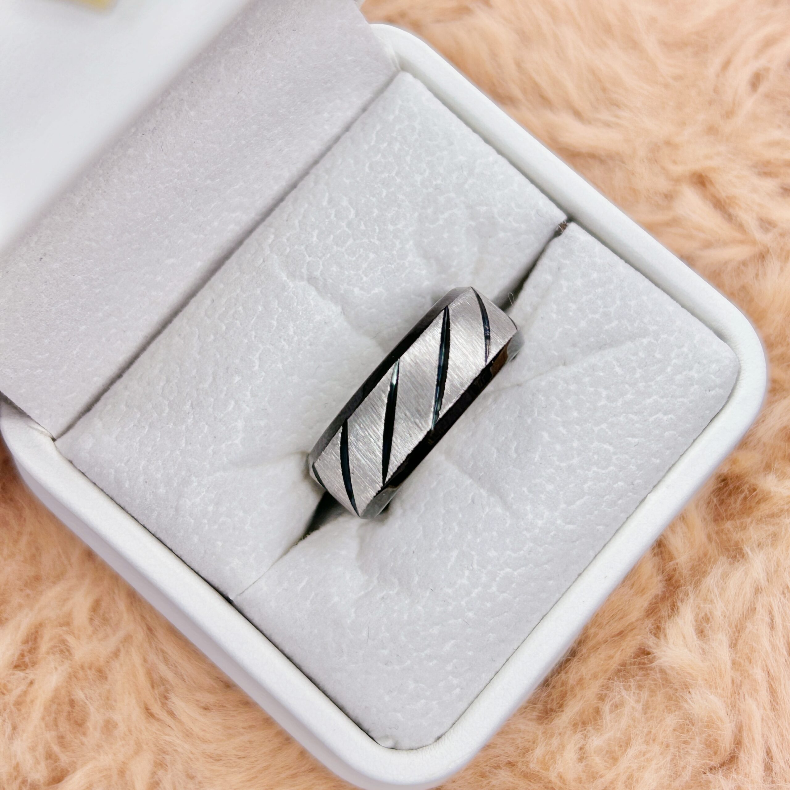 Close-up of a light gray foam cushion inside a white box, with orange fur along the edges and a small metal clasp with black cords resting on it.