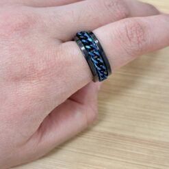 Close-up of a black metal bracelet with a blue braided chain on a wrist.
