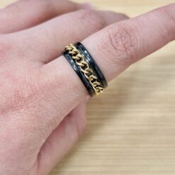 Close-up of a finger wearing a black enamel ring with a gold chain detail.