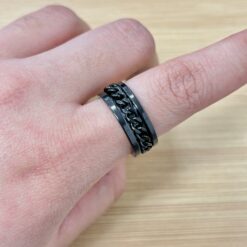 Close-up of a person's wrist wearing a glossy black metal chain bracelet, resting on a light wood surface.