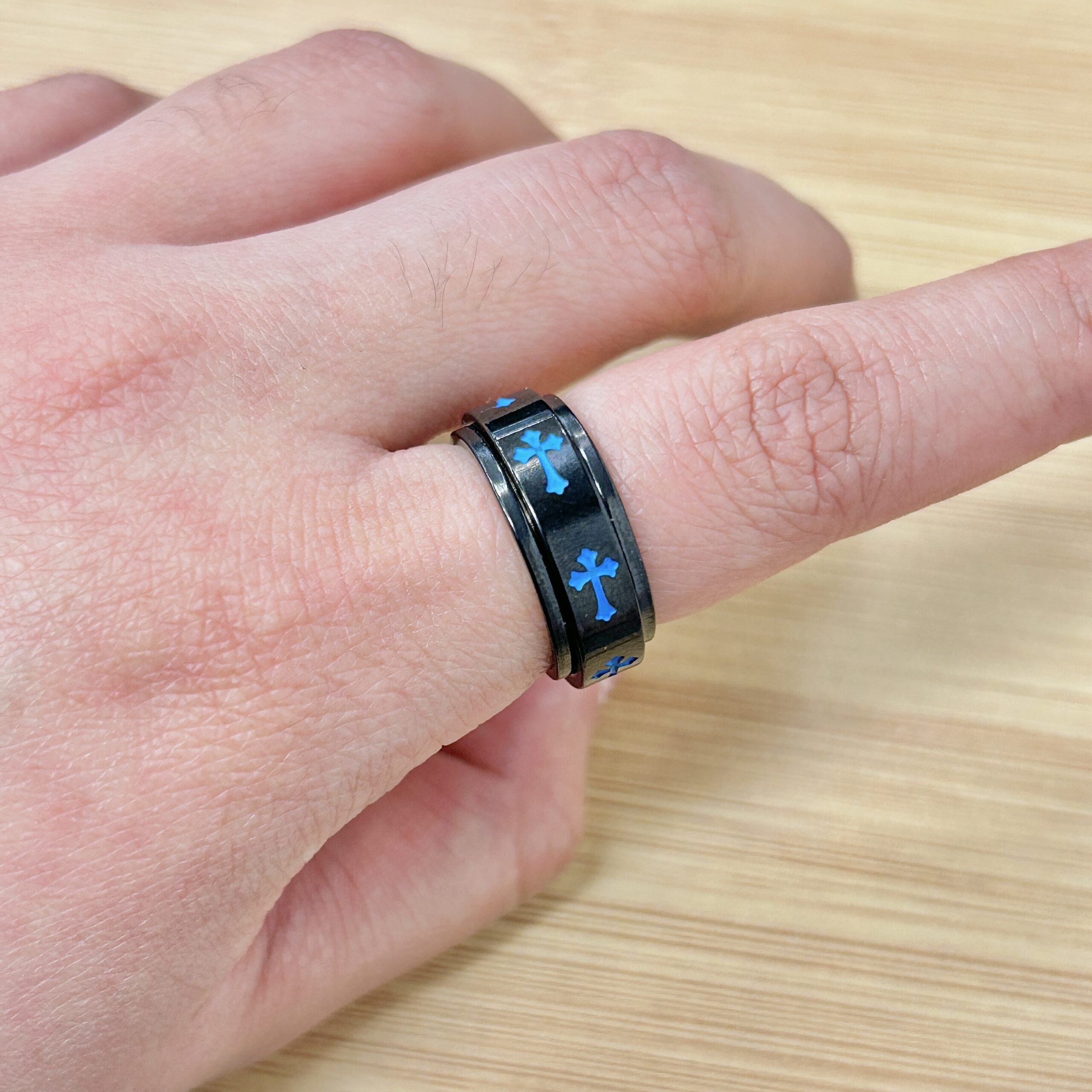 Close-up of a wrist wearing a black bracelet with blue cross-shaped inlays on a wooden surface.