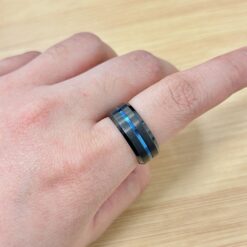 Close-up of a finger wearing a gray metal ring with a blue inlay on the skin, wooden table in the background.