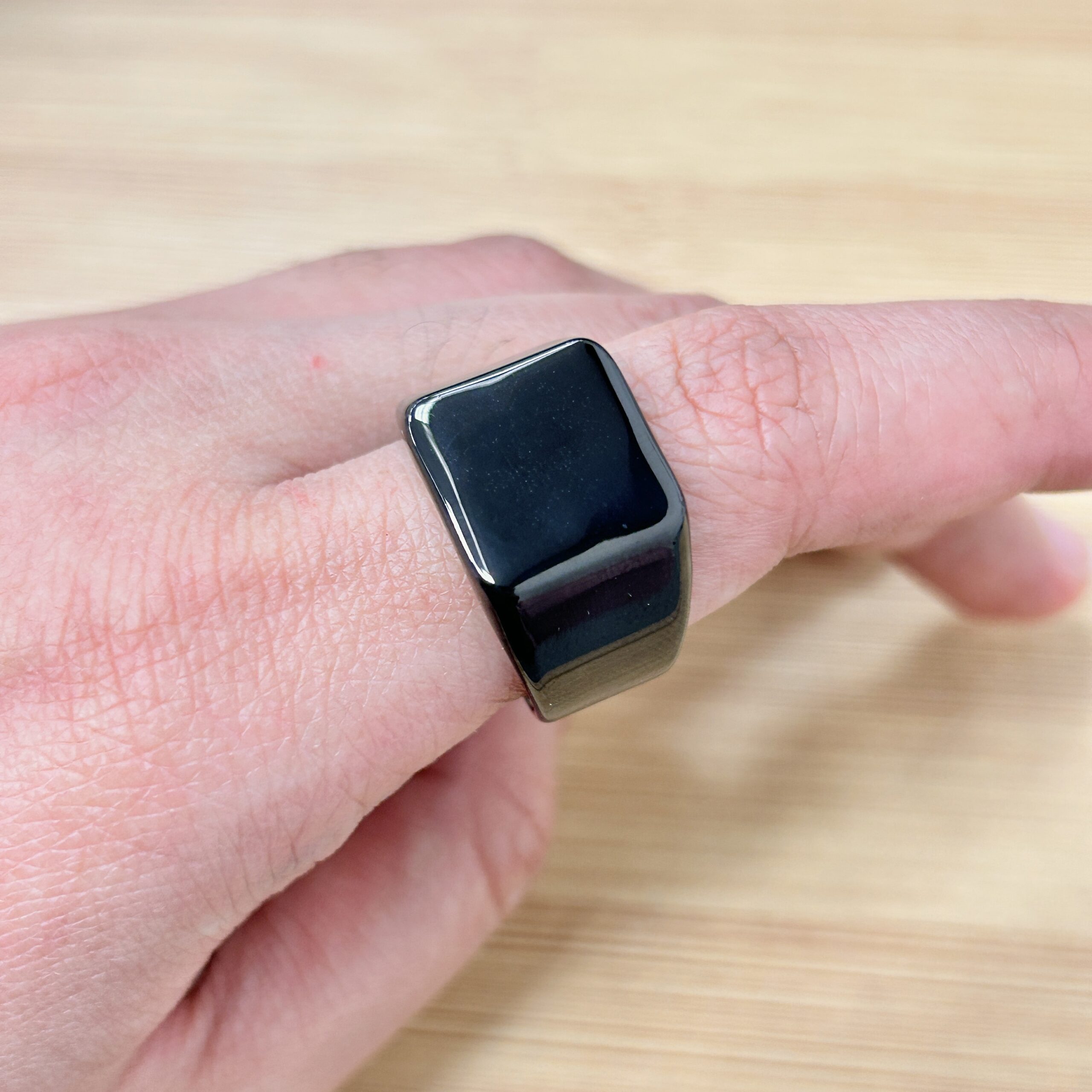 Close-up of a black smartwatch on a person's wrist, resting above a wooden surface. It has a glossy screen and a dark band.