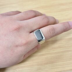 Close-up of a silver rectangular ring on a finger resting on a light wooden surface.