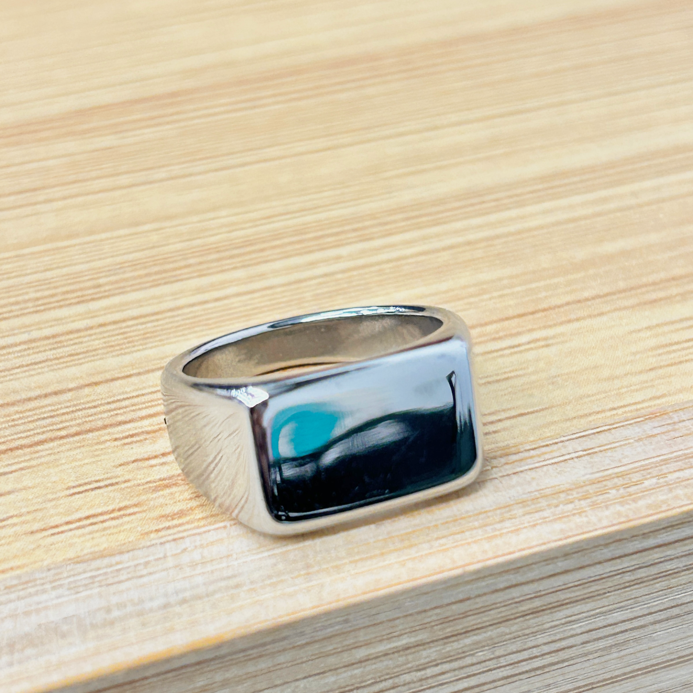 Bold Silver Square Shiny Statement Ring picture2 - Eriy Gift Close-up of a shiny chrome handle resting on a light wooden table surface I think this is a metal hardware piece.