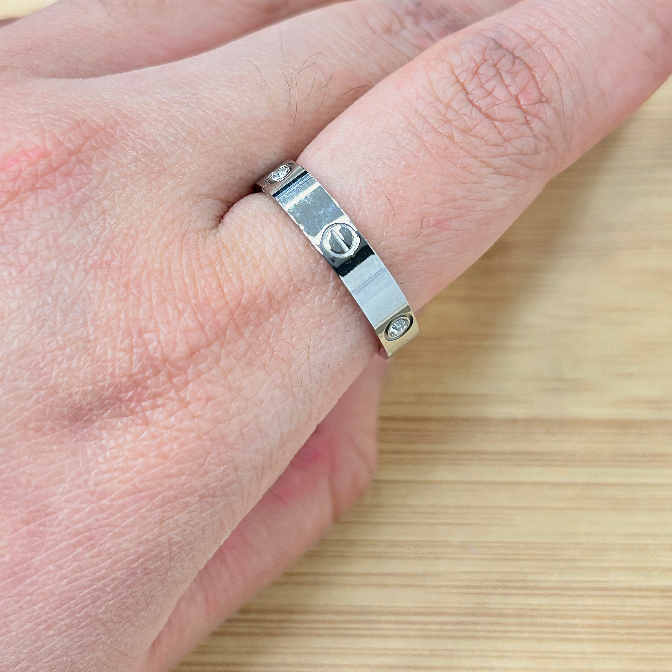 Close-up of a silver ring with rivet-like accents on a finger, against a light wooden background.