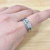 Close-up of a finger wearing a wide silver ring with engraved symbols, against a light wooden surface.