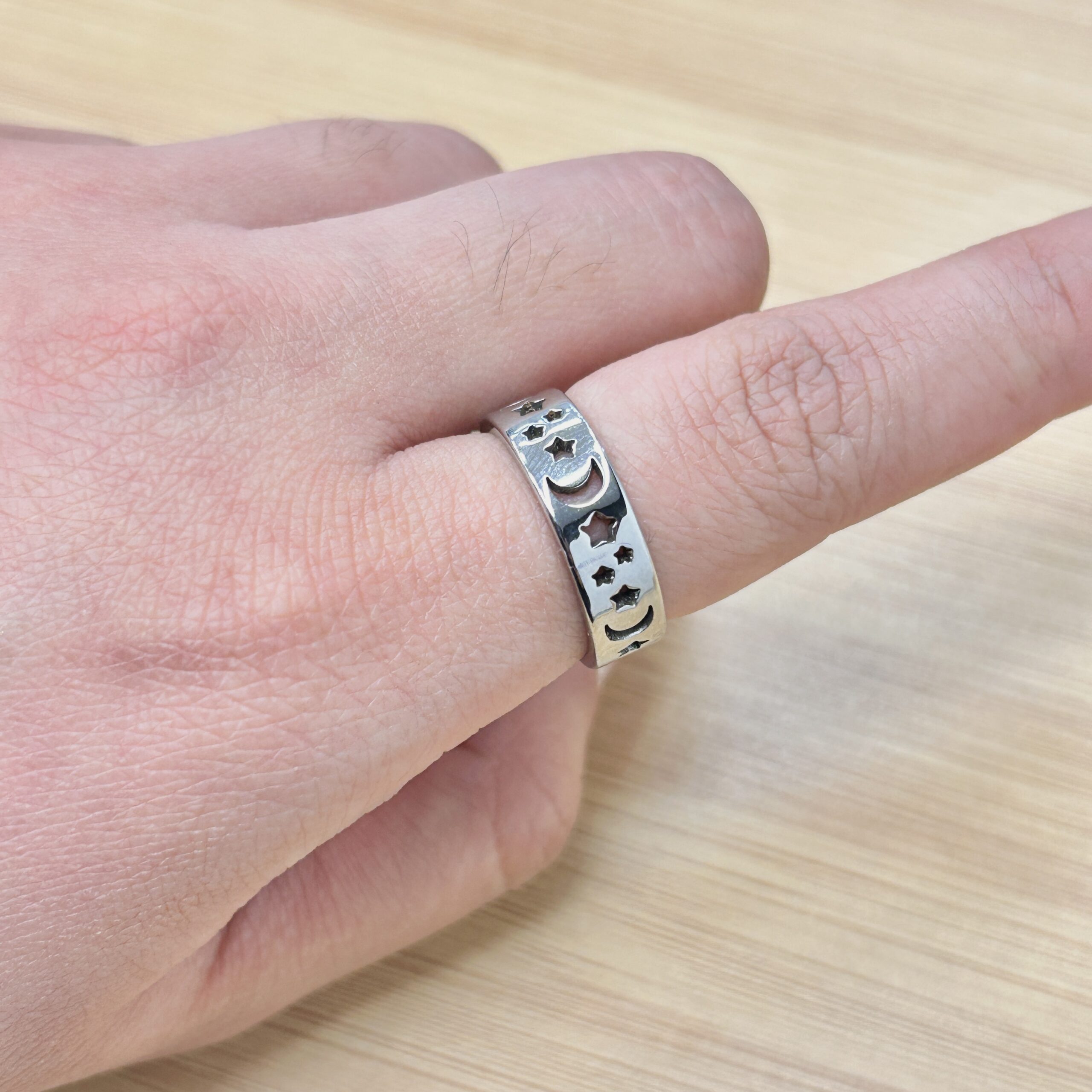 Dainty Silver Celestial Moon Star Hollow Ring - Eriy Gift Close-up of a hand wearing a silver decorative ring with star and crescent shapes on the ring finger, against a wooden background.