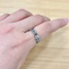 Close-up of a person's wrist with a silver circular-link bracelet and a decorative ring on a light wooden surface (skin detail visible).