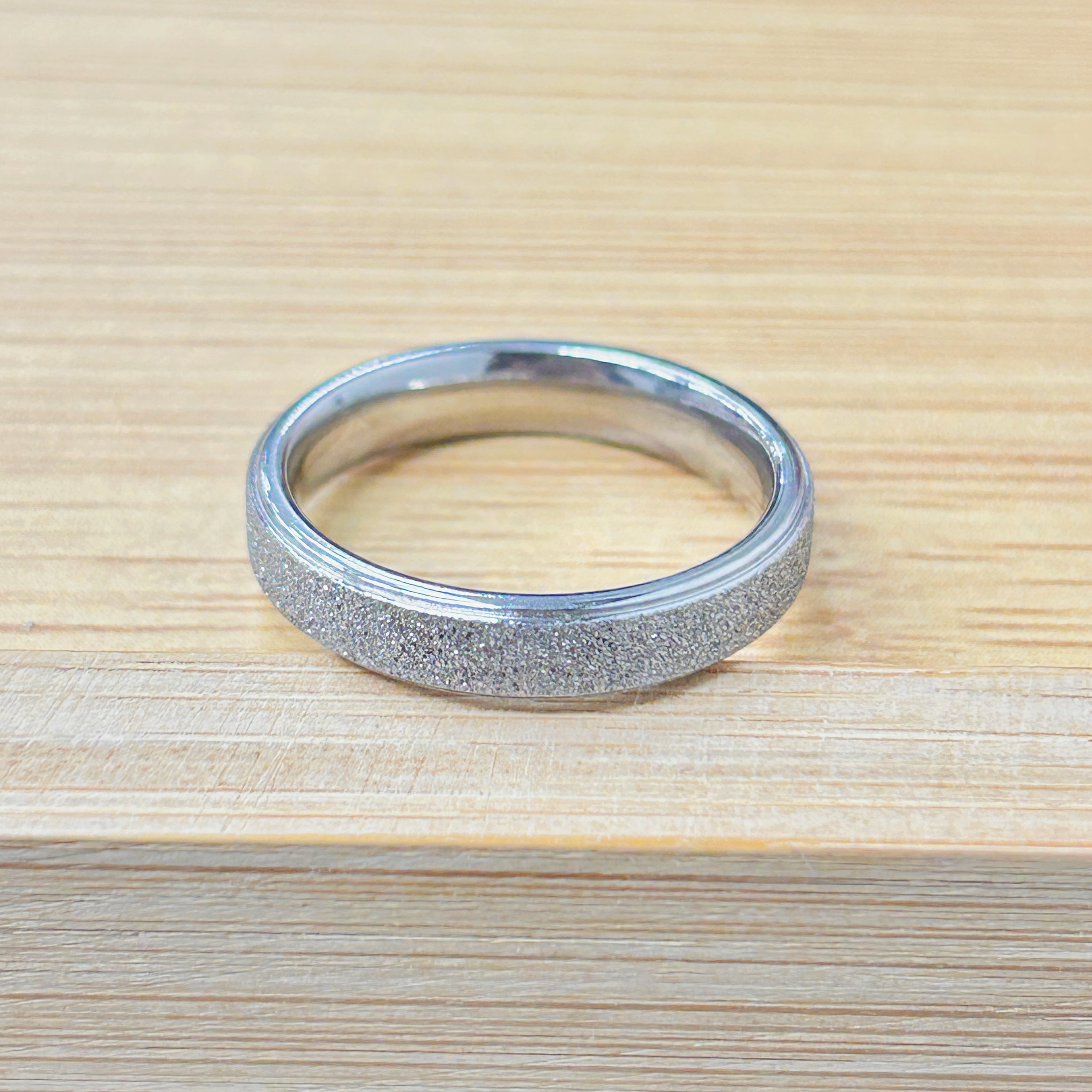 Close-up of a shiny metal circular ring lying on a light wood surface, showing its inner opening and textured exterior edges.