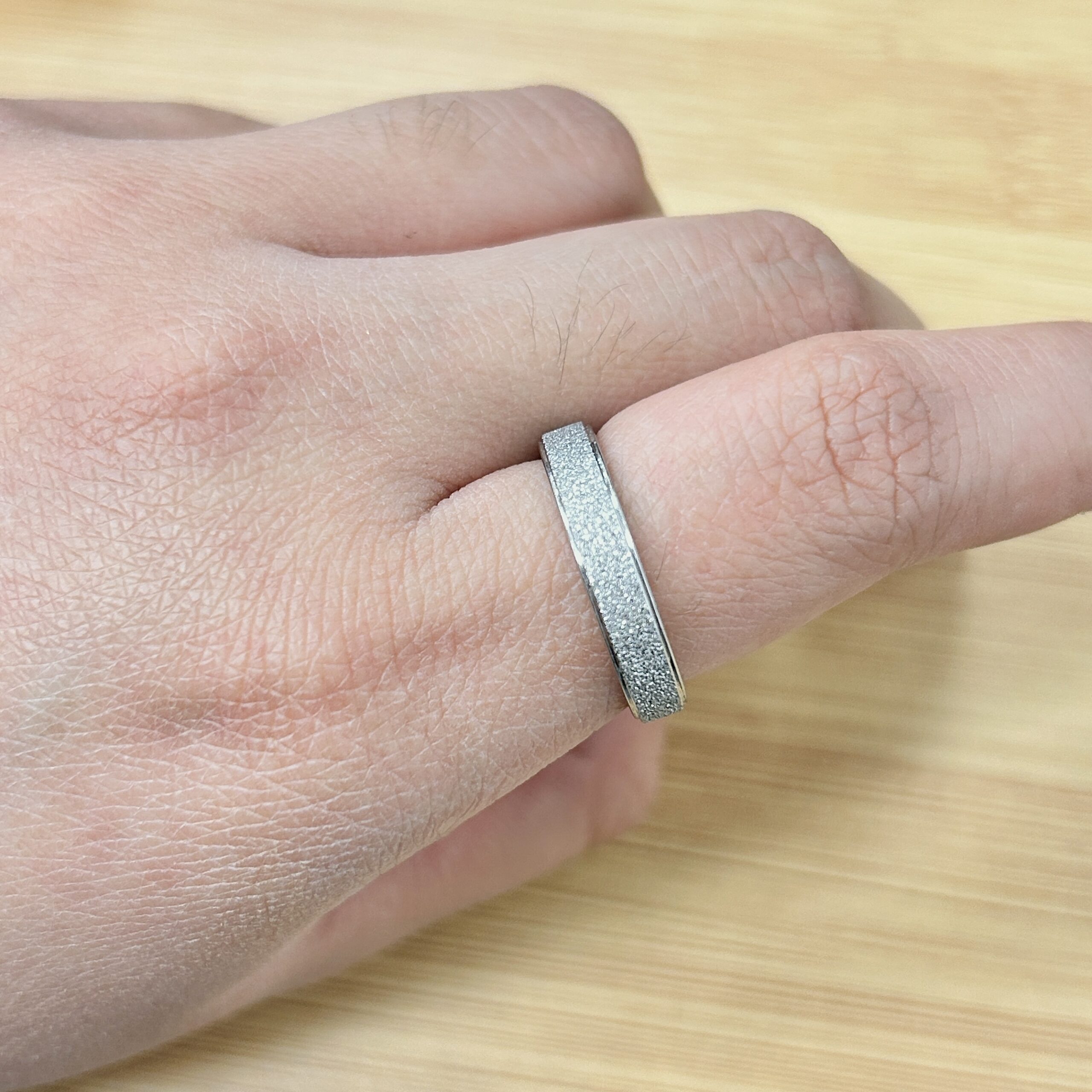 Dainty Silver Sandblast Glitter Promise Ring - Eriy Gift Close-up of a textured silver ring worn on a finger, with a light wooden surface in the background.