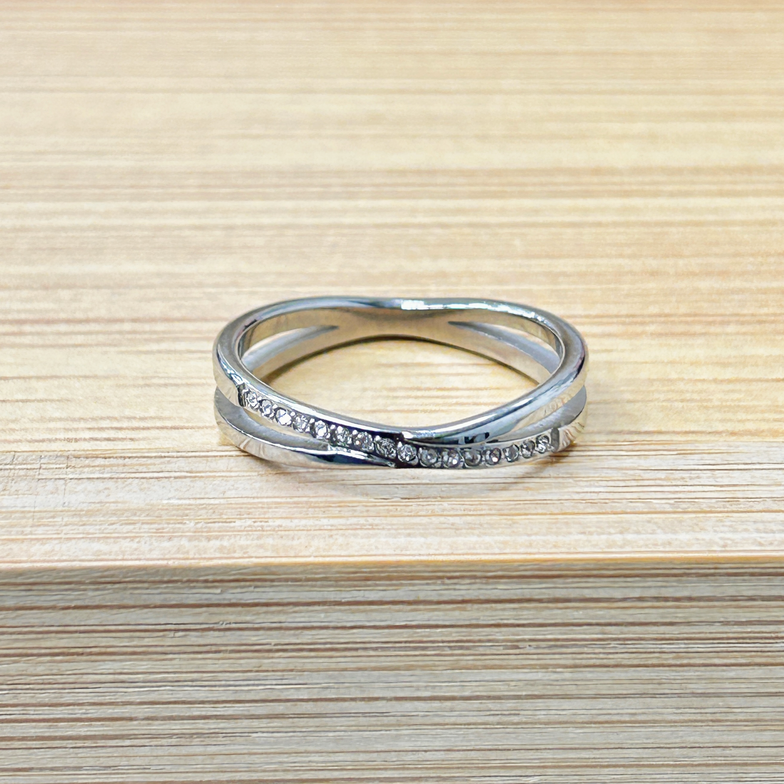 Stack of silver rings resting on a light wooden surface, one ring with small stones.