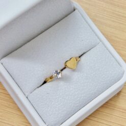 Rose-gold ring with a large central gemstone in a gray jewelry box on a wooden table.