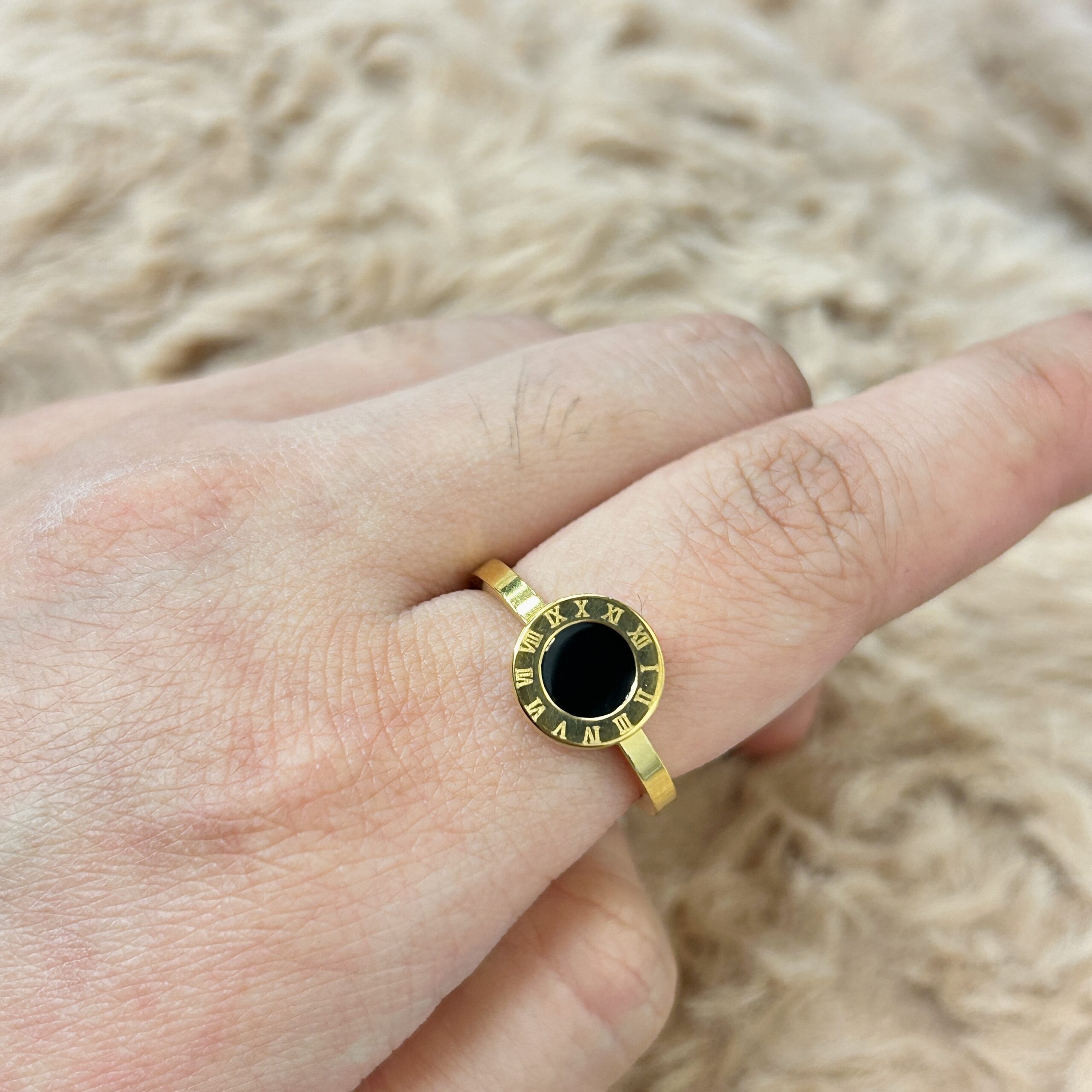 Gold-tone bracelet with a circular black onyx centerpiece bordered by Roman numerals, worn on the wrist.