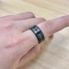 Close-up of a finger wearing a dark, segmented metal ring on a light wooden surface.