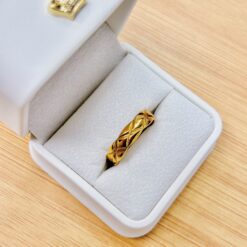 Gold ring resting in a gray padded jewelry box on a wood surface