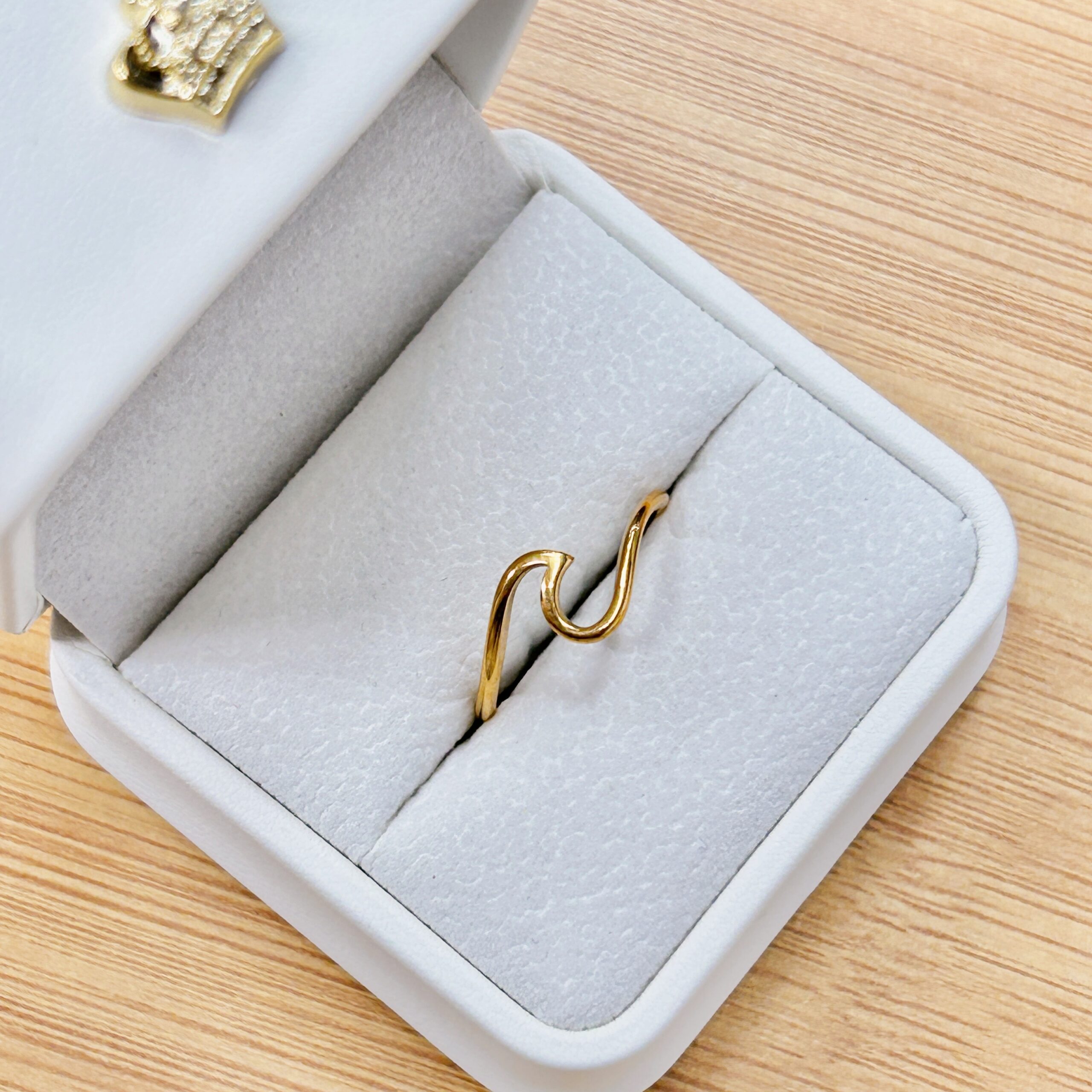 Close-up of a gold wedding band inside a gray velvet jewelry box on a wooden surface.