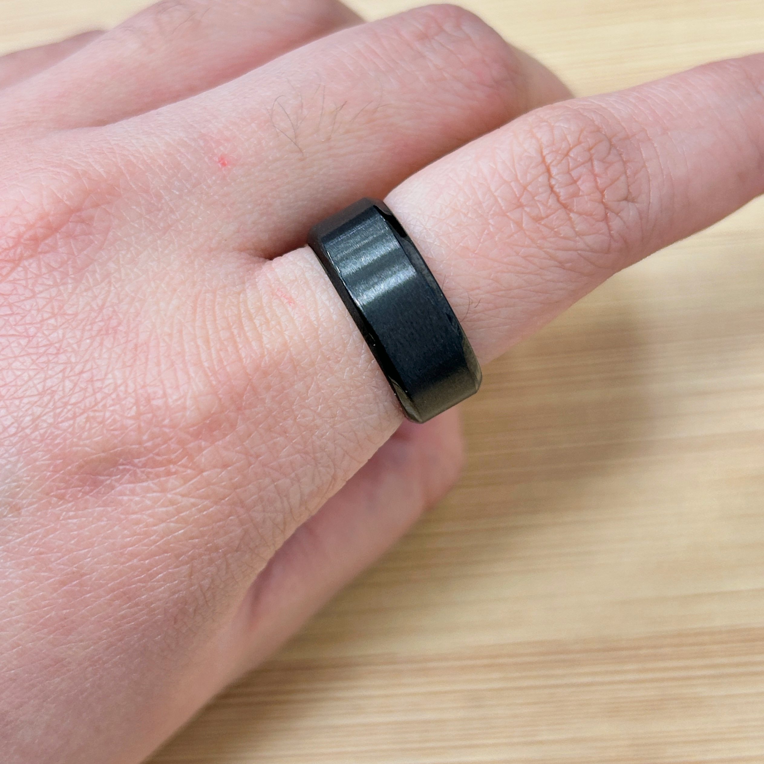 Minimalist Matte Black Plain Chunky Ring - Eriy Gift Close-up of a finger wearing a black ring, showing skin texture and a small red blemish on the skin nearby.