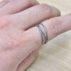 Close-up of a hand wearing three silver band rings on the finger, with visible skin texture and fine hairs.