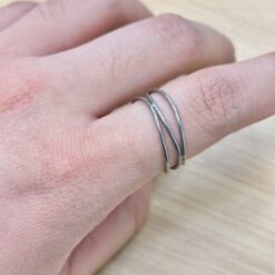 Minimalist Silver Crisscross Intertwined Ring - Eriy Gift Close-up of a hand wearing three silver band rings on the finger, with visible skin texture and fine hairs.
