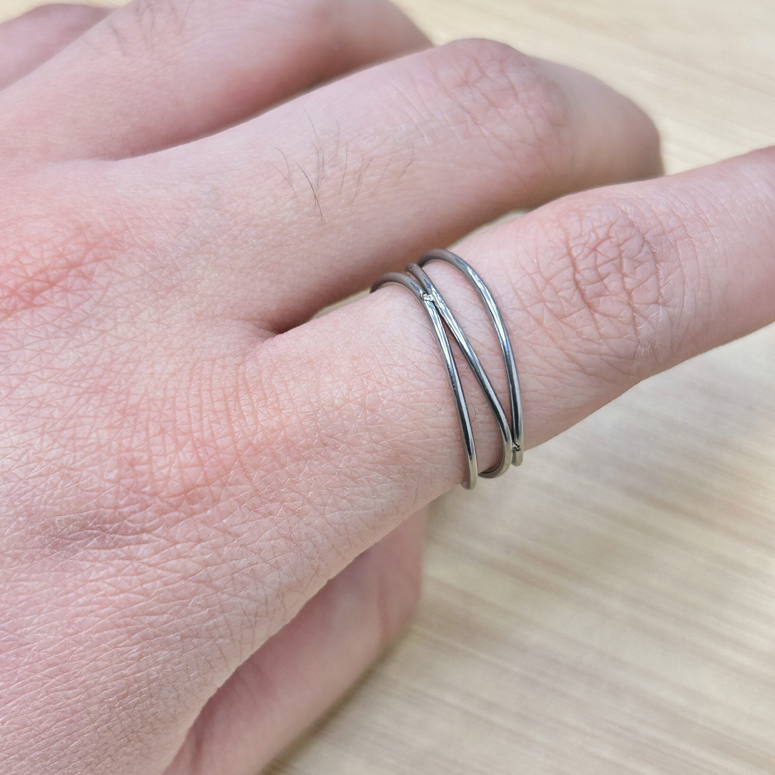 Minimalist Silver Crisscross Intertwined Ring - Eriy Gift Close-up of a hand wearing three silver band rings on the finger, with visible skin texture and fine hairs.