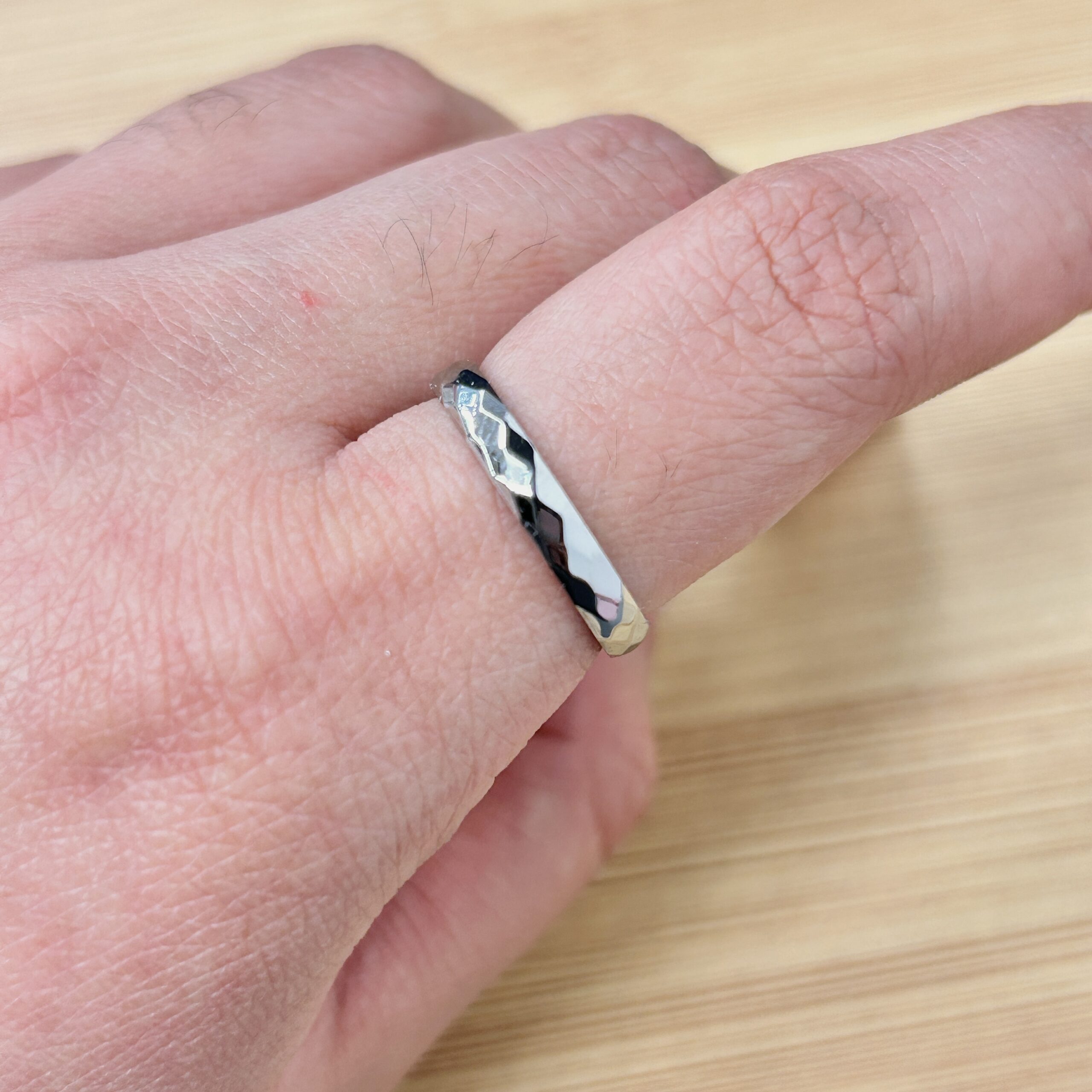 Close-up of a finger wearing a chunky silver ring with a dark central stone on a light wooden surface.
