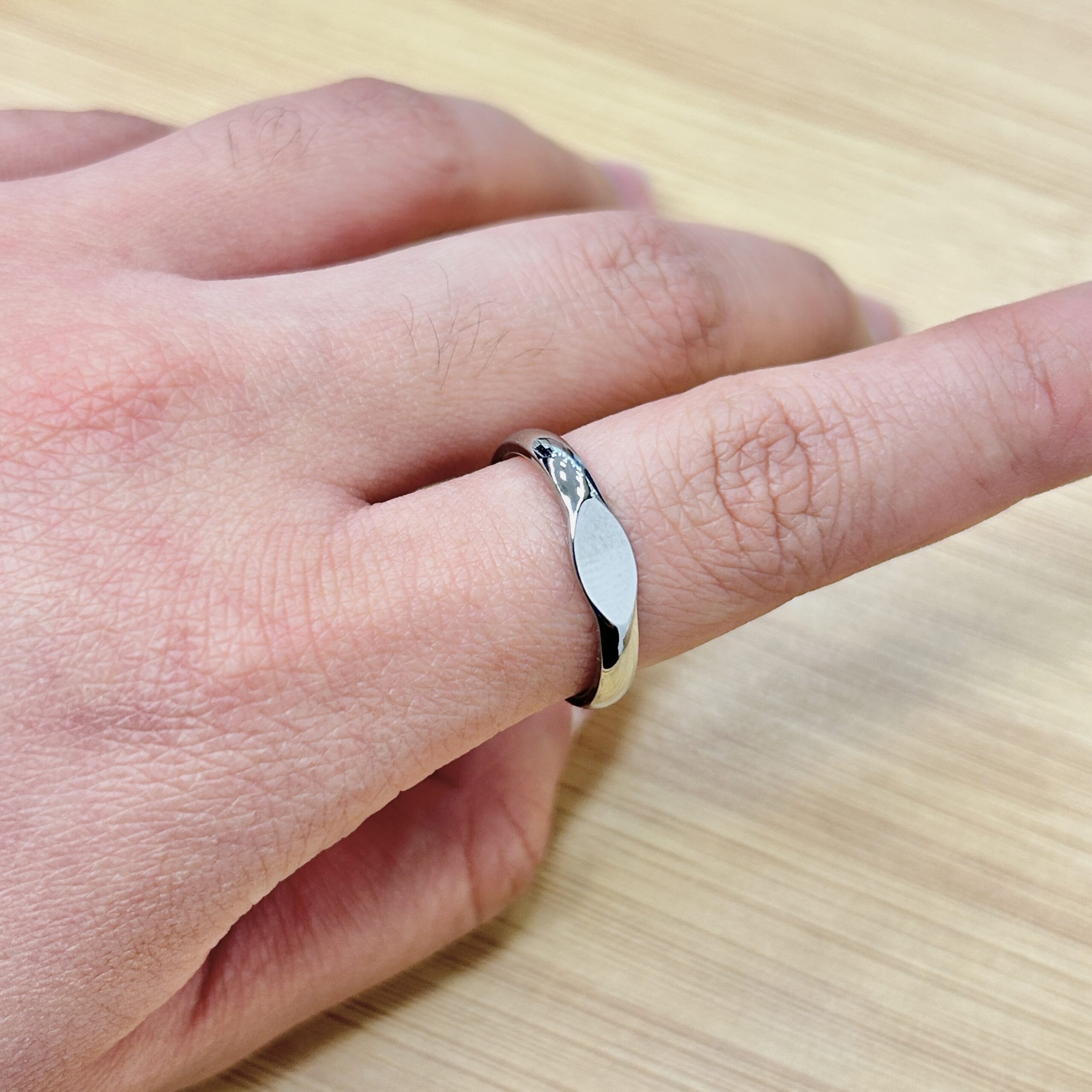 Close-up of a finger wearing a silver ring with a blue stone, resting on a light wooden surface.