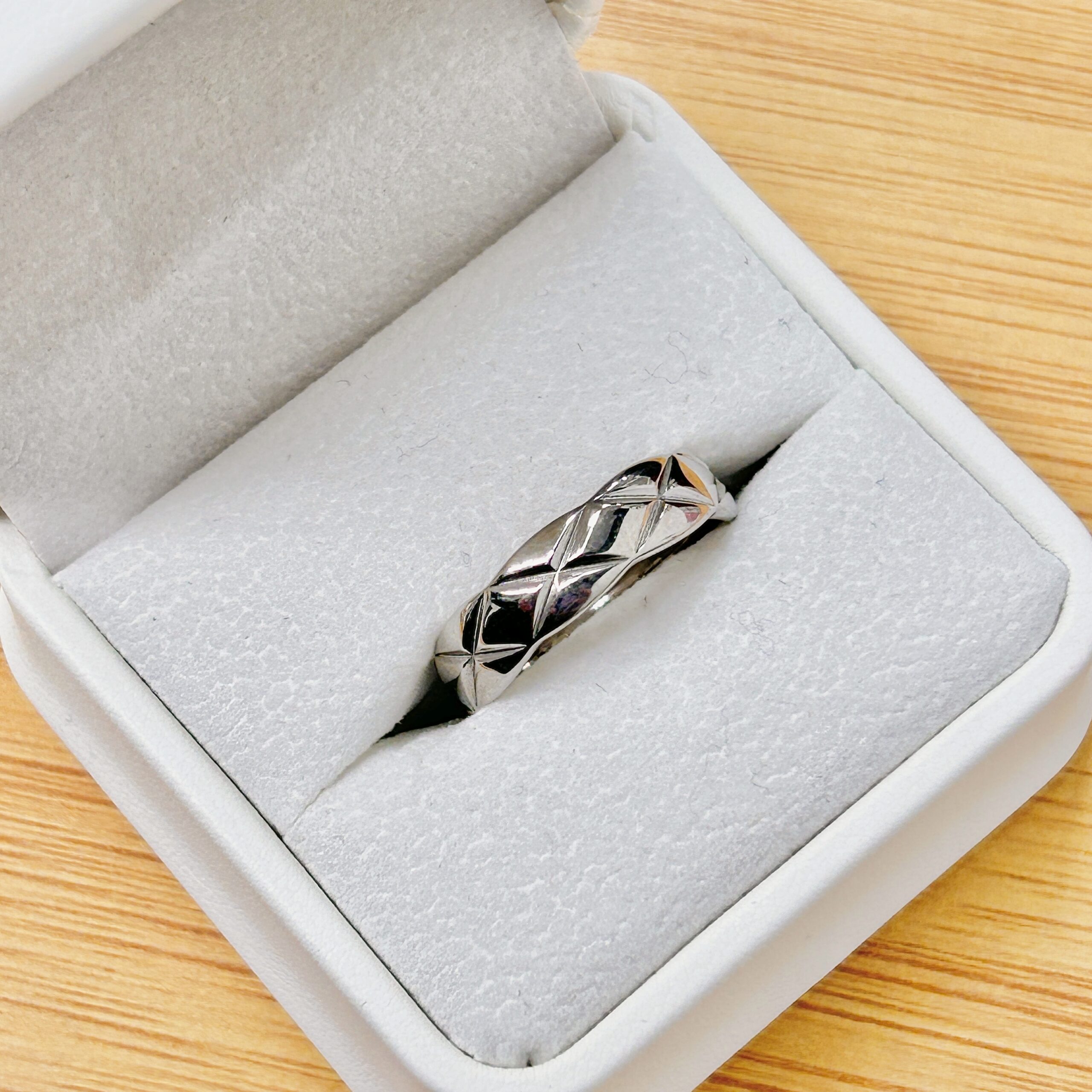 Close-up of a silver ring with geometric facets in an open gray jewelry box on a wooden table.