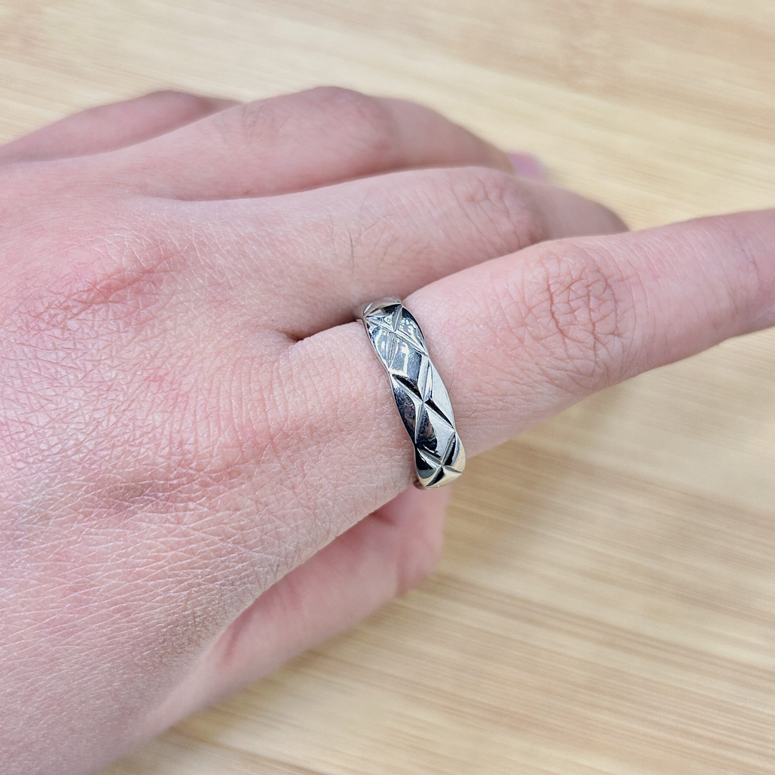 Close-up of a hand wearing a silver patterned ring on the ring finger, with a light wooden surface in the background