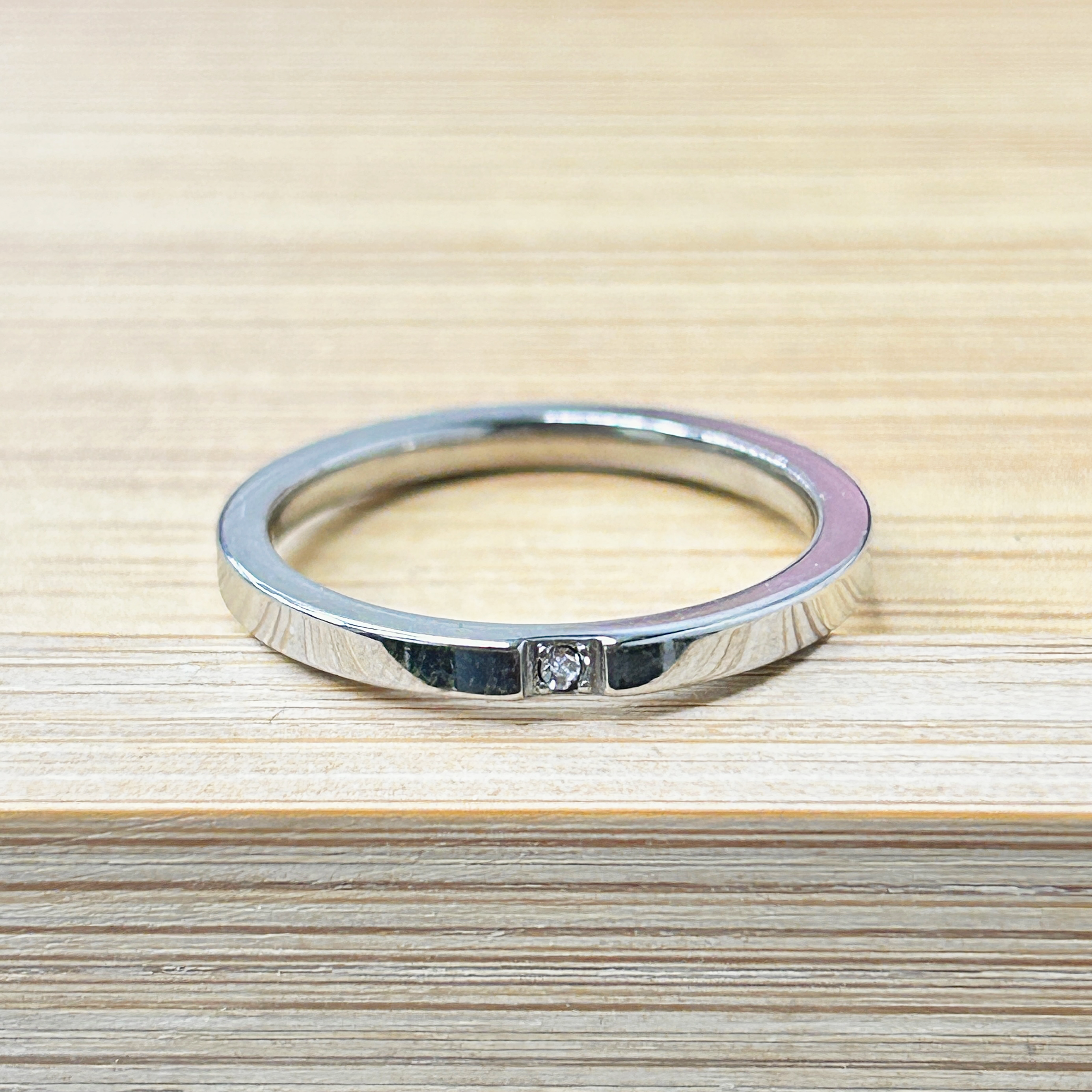 Circular metal ring resting on a light wooden surface, with a small latch visible at the bottom edge.