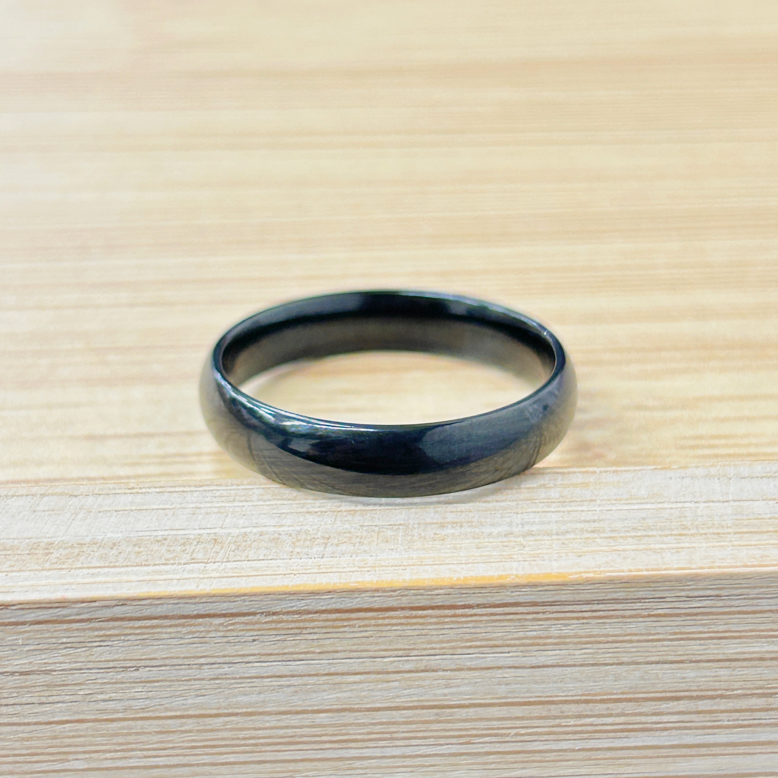 Minimalist Thick Black Stackable Ring picture2 - Eriy Gift Close-up of a black metal ring resting on a light wooden table.