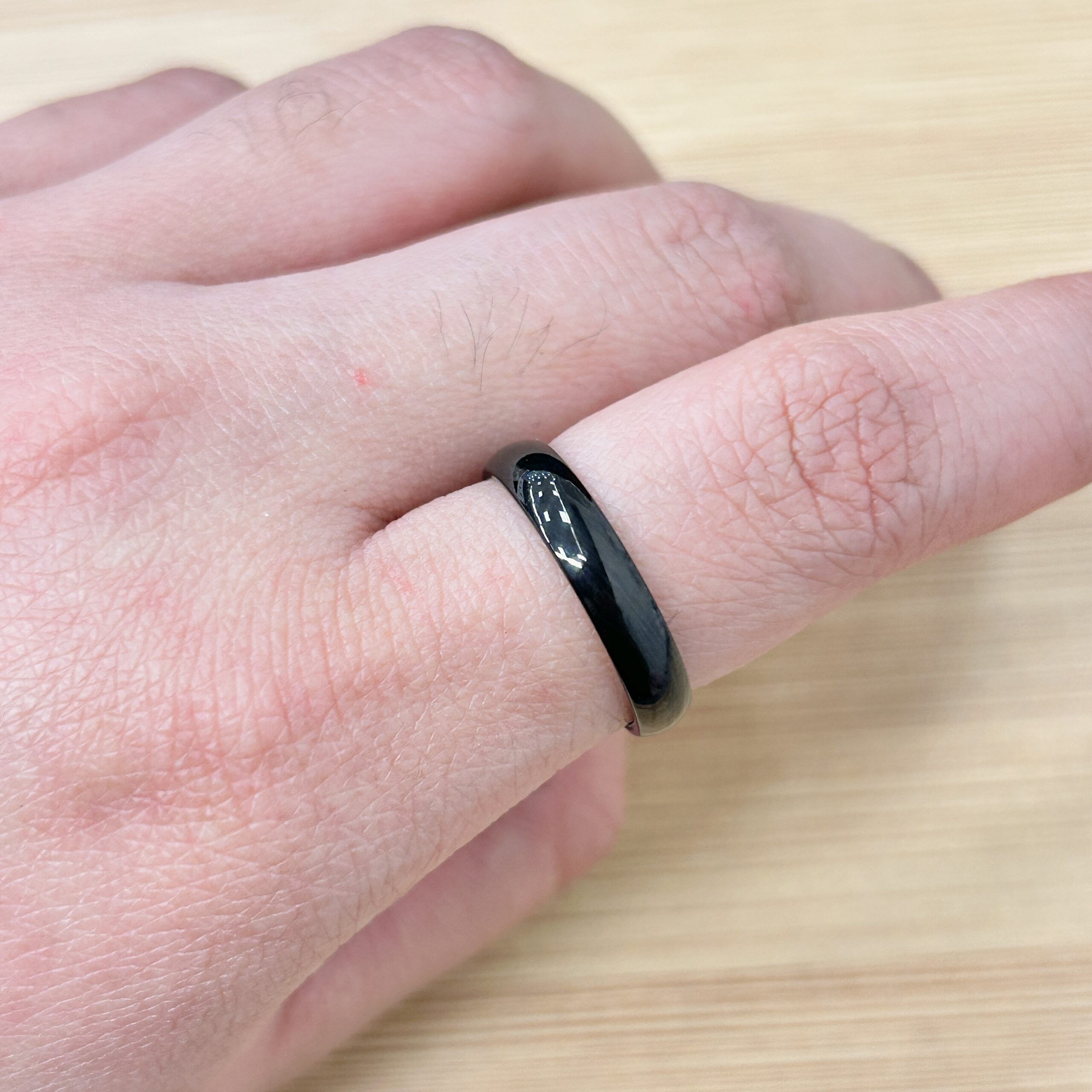 Minimalist Thick Black Stackable Ring - Eriy Gift Close-up of a finger wearing a black, glossy ring with white accents on a wooden surface.
