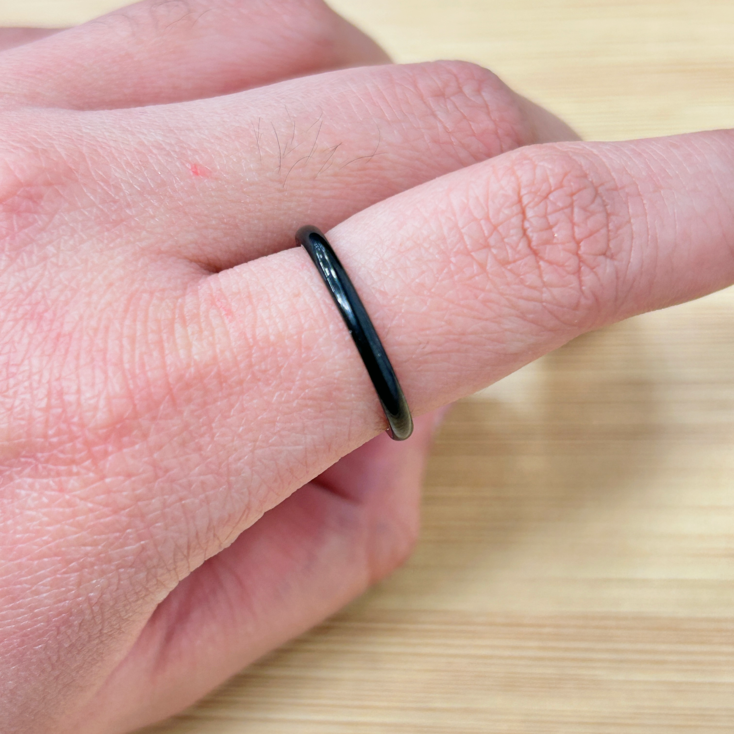 Minimalist Thin Black Stackable Ring - Eriy Gift Close-up of a hand wearing a glossy black ring on the finger, with a light wooden surface in the background.