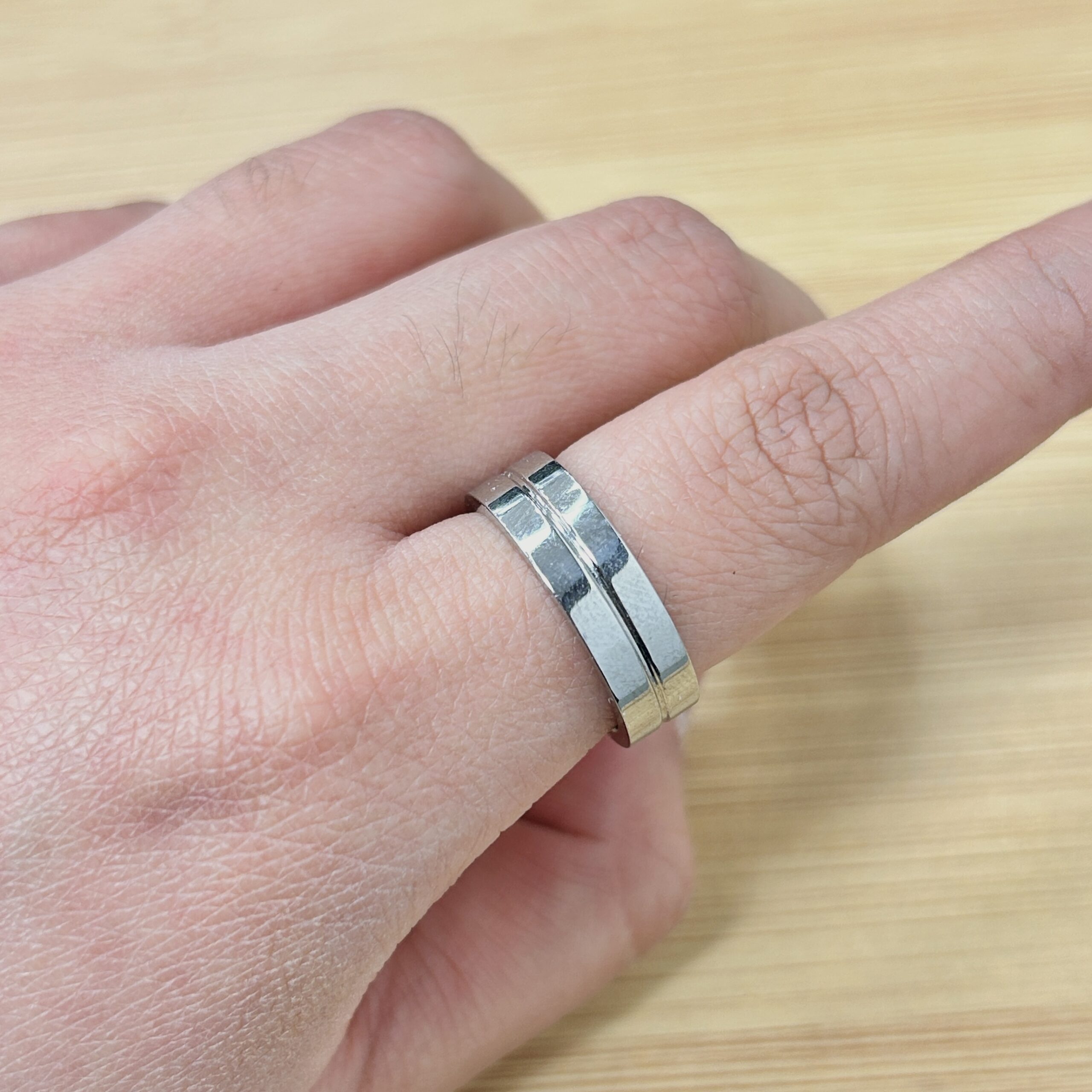 Polished Silver Center Groove Band Ring - Eriy Gift Close-up of a finger wearing a chunky silver band ring against a light wooden surface.