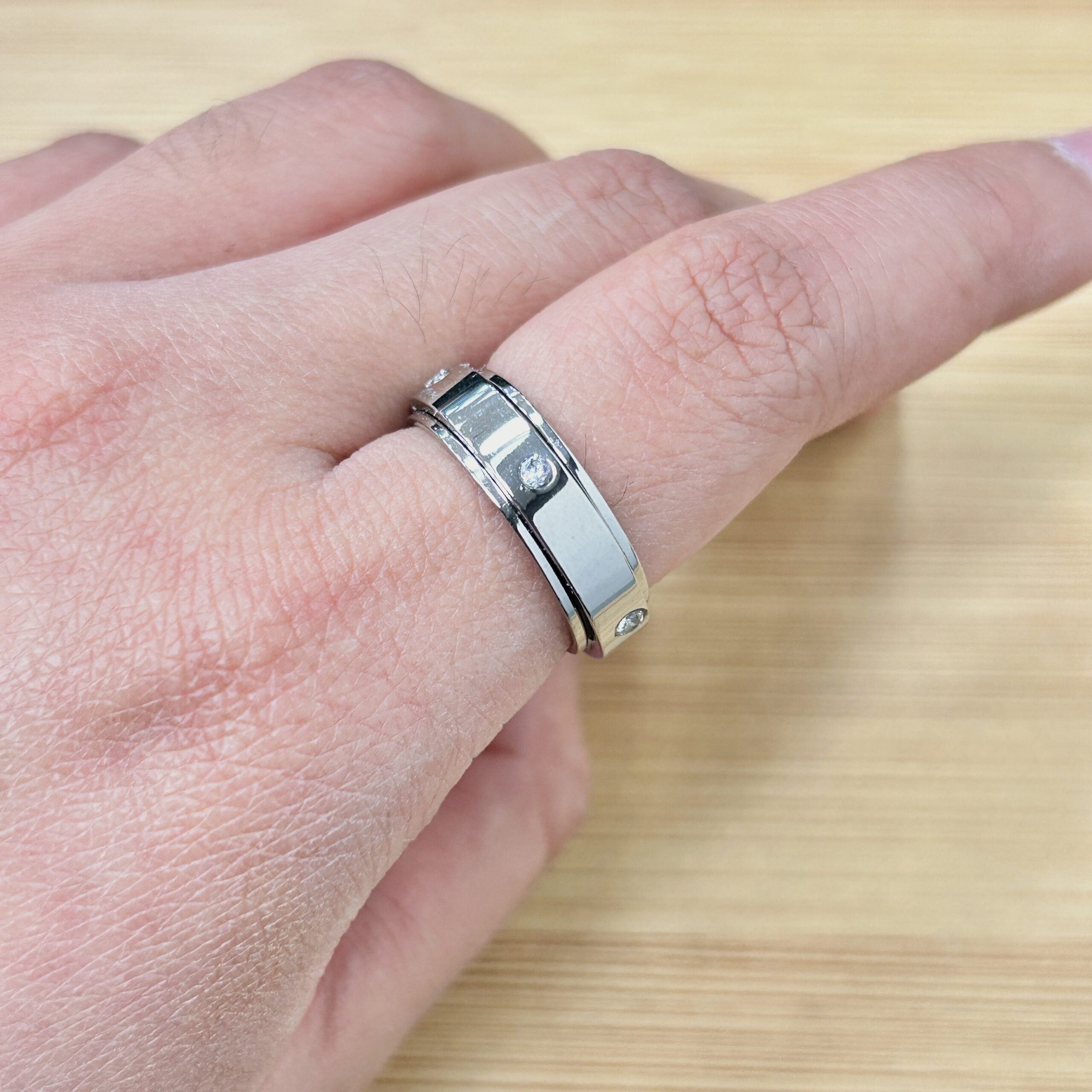 Silver Band Zircon Studded Spinner Ring - Eriy Gift Close-up of a wrist wearing a silver metal watch band, with a ring on the finger and a light wood background.
