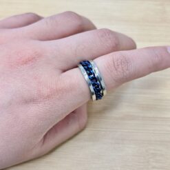 Silver Blue Spinning Cuban Link Chain Ring - Eriy Gift Close-up of a hand wearing a silver ring with a blue braided inlay on a light wooden surface.