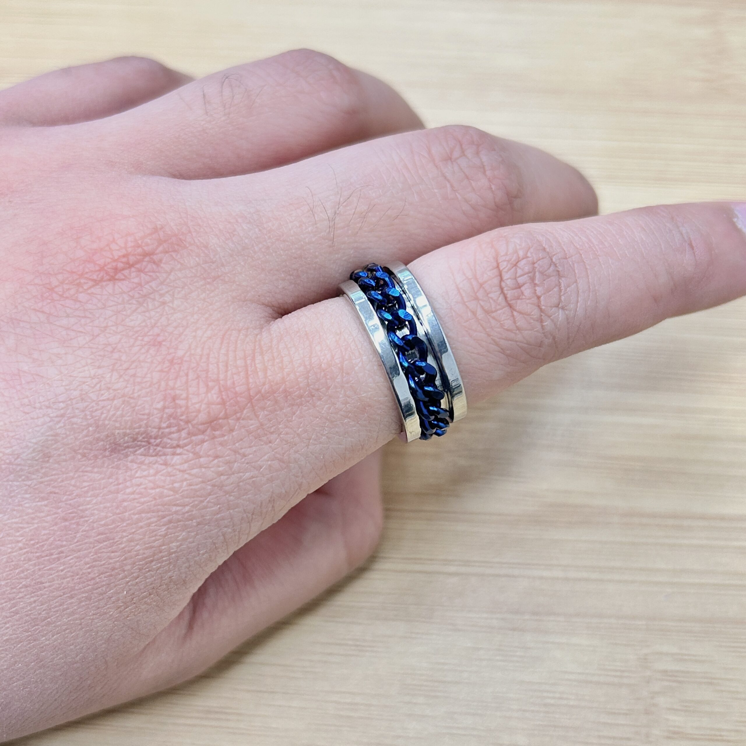 Silver Blue Spinning Cuban Link Chain Ring - Eriy Gift Close-up of a hand wearing a silver ring with a blue braided inlay on a light wooden surface.