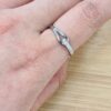 Close-up of a finger wearing a silver diamond-studded ring, with a metal jewelry tool near the band.