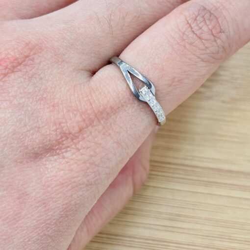 Silver Buckle Design Zircon Stackable Ring - Eriy Gift Close-up of a finger wearing a silver diamond-studded ring, with a metal jewelry tool near the band.