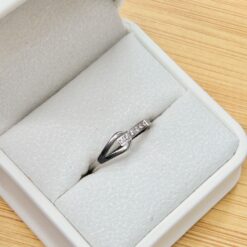 Close-up of a silver ring in a gray velvet jewelry box on a wooden surface.